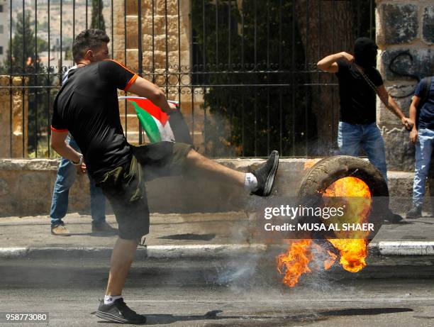 Palestinian kicks a flaming tire towards Israeli security forces during clashes after a protest marking the 70th anniversary of Nakba -- also known...