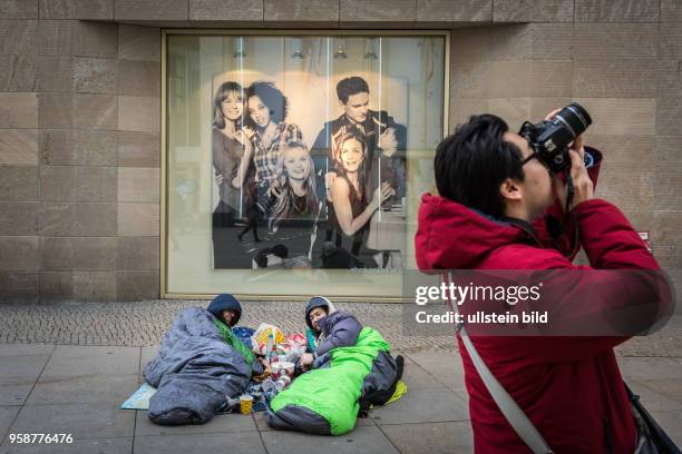 Deutschland Germany Berlin Zwei Obdachlose liegen vor einer Kaufhauswerbung auf dem Alexanderplatz. Ein Tourist fotografiert den Alex.