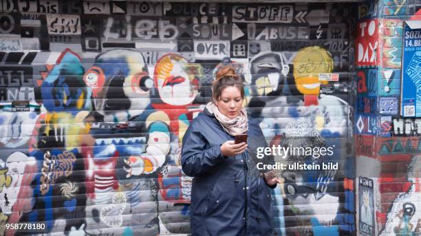 Junge Frau steht vor einer bunt besprayten Graffity-Wand im Viertel in Bremen und schaut auf ihr Handy,