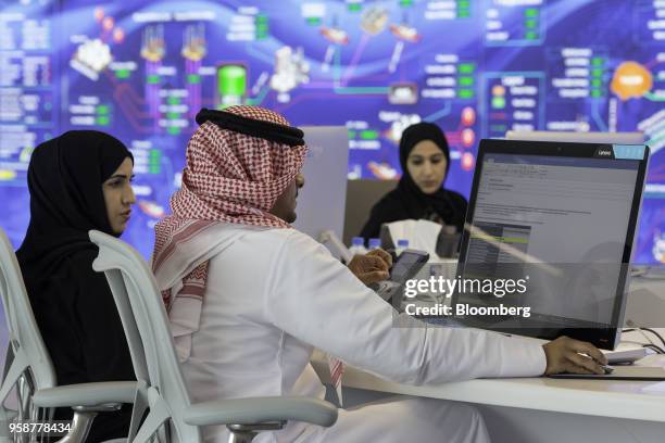 Male and female employees work in front of a digital screen displaying data relating to oil and gas flows in the Panorama Command Center at the Abu...