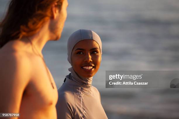 black muslim girl wearing hijab talking with a man before surfing - thisisaustralia stock-fotos und bilder