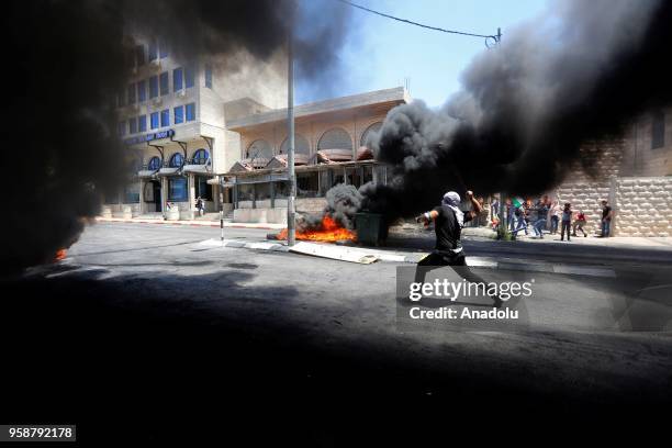 Palestinian protestors burn tyres and throw rocks with slingshots in response to Israeli forces' intervention during a protest, organized to mark...