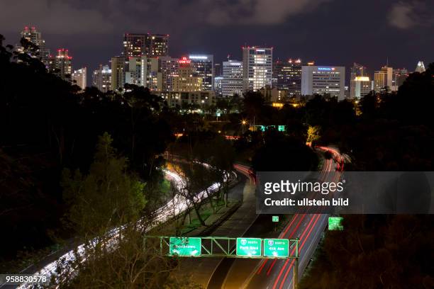Longish automobile light trails of the traffic on a street leading to the illuminated Downtown San Diego skyline.