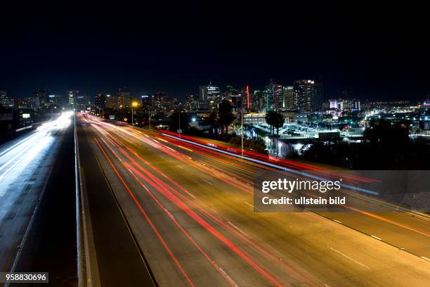 Longish automobile light trails of the traffic at the Interstate 5 leading to the illuminated Downtown San Diego skyline.