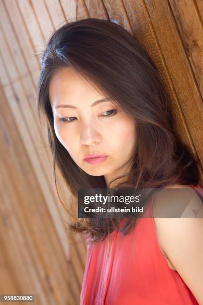 Japanese woman with red top leaning on a wooden wall in Pacific Beach.