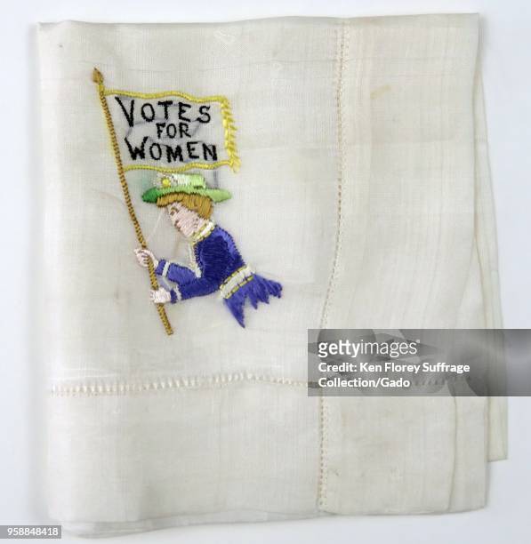 White handkerchief, folded in a square, with green, purple, and white embroidery depicting a woman from the waist-up, holding a flag with the message...