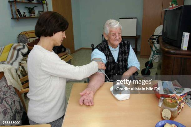 Deutschland, Brandenburg, Rentnerin in ihrem Zimmer im Pflegeheim in Letschin. Pflegerin misst den Blutdruck mit einem Blutdruckmessgerät