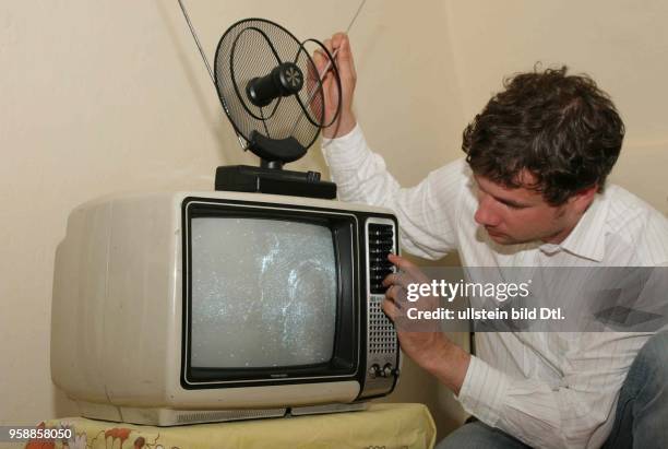 Mann versucht in seinem alten Fernseher mit Zimmerantenne einen Sender einzustellen