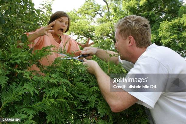 Symbolfoto Nachbarschaftsstreit, Streit am Gartenzaun, Frau streitet mit dem Nachbarn beim Hecke schneiden.