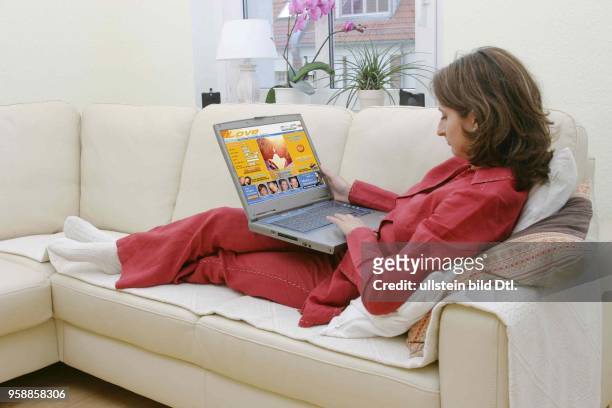 Deutschland, Internethandel, Online-Shopping, Frau sitzt zuhause auf dem Sofa und surft mit Notebook im Internet auf einer Seite für...
