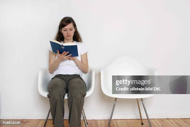 Deutschland, Symbol warten, Wartezimmer, junge Frau sitzt auf einem weissen Stuhl und liest ein Buch