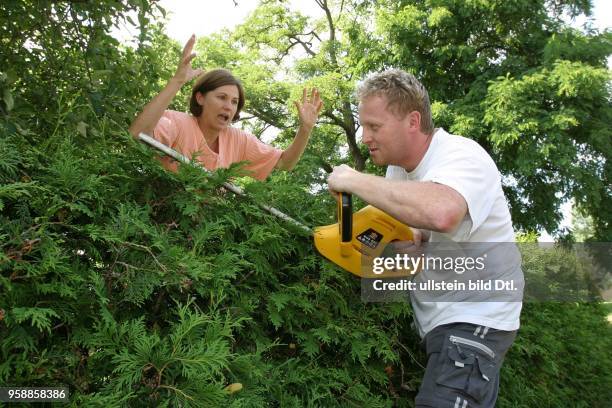 Symbolfoto Nachbarschaftsstreit, Streit am Gartenzaun, Frau streitet mit dem Nachbarn beim Hecke schneiden.