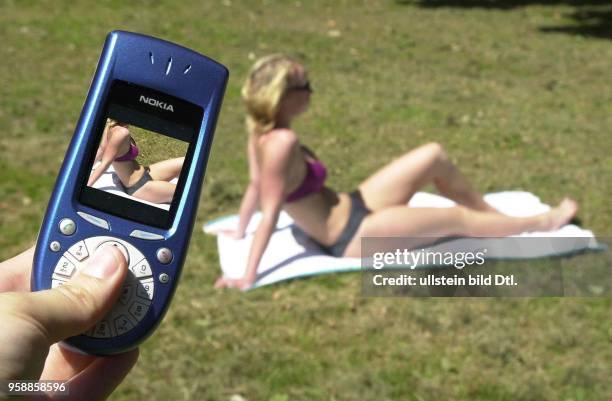 Fotohandy, Spanner fotografiert ein Maedchen im Bikini auf einer Wiese.