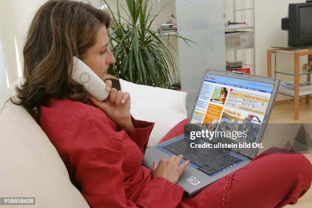 Deutschland, Internethandel, Online-Shopping, Frau sitzt zuhause auf dem Sofa und surft mit Notebook im Internet auf der Seite des Reiseanbieters TUI...