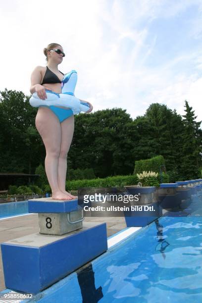 Junge Frau im Bikini mit Schwimmring und Schwimmbrille steht auf einem Startblock am Beckenrand im Poseidon-Freibad