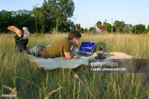 Altlewin, Brandenburg, DEU - Mann liegt auf einer Wiese und guckt auf seinem Laptop Fernsehen. (DVB-T, Digital Video Broadcasting - Terrestrial,...