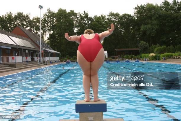 Junge Frau im Badeanzug springt von einem Startblock am Beckenrand im Poseidon-Freibad