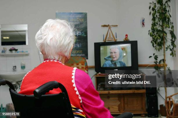 Altenheim, Altenpflege, Rentnerin im Altersheim sitzt im Rollstuhl und schaut Fernsehen -