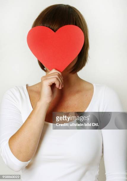 Symbolic photo love, single, looking for a partner, woman with a red heart in front of her face -