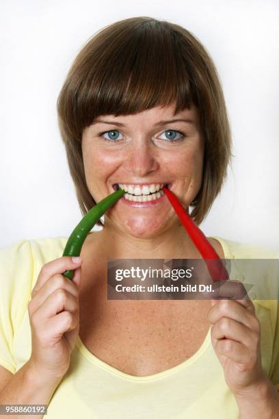 Germany; young woman biting in two chilis - 2007