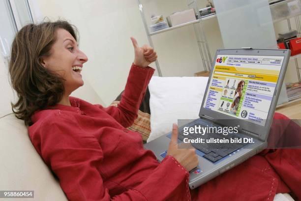 Deutschland, Internethandel, Online-Shopping, Frau sitzt zuhause auf dem Sofa und surft mit Notebook im Internet auf der Seite des...