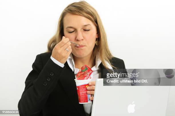 Young woman is working at an apple laptop and is eating a joghurt -