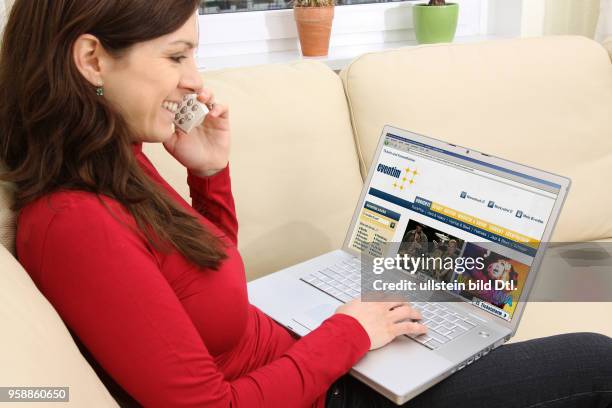 Woman with laptop sitting on the sofa is surfing in the internet on the homepage of the ticket vendor Eventim -