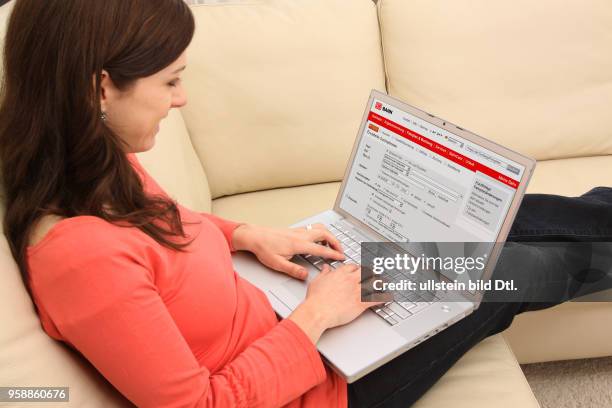 Woman with laptop sitting on the sofa is surfing in the internet and is booking a railway ticket on the homepage of the German Reilway -
