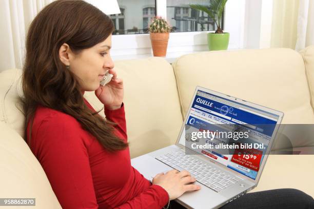 Woman with laptop sitting on the sofa is surfing in the internet on the homepage of mail order company Quelle -