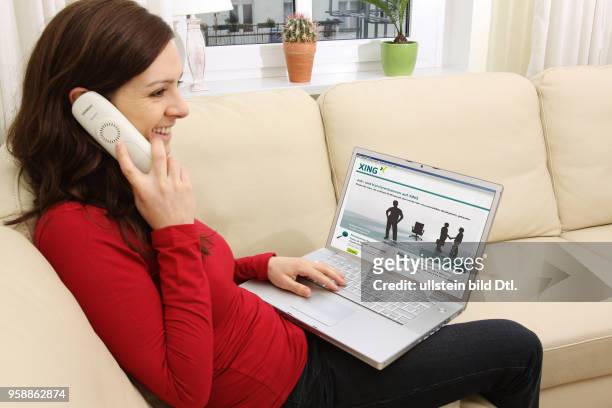 Woman with laptop sitting on the sofa is surfing in the internet on the homepage of the business contact platform XING -
