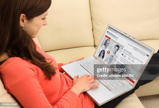 Woman with laptop sitting on the sofa is surfing in the internet on the homepage of the dating agency ElitePartner -