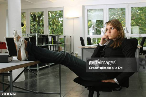 Young woman is working in the office, putting her feet up and making a phone call -