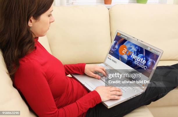 Woman with laptop sitting on the sofa is surfing in the internet on the homepage of the heute news broadcast of the ZDF -