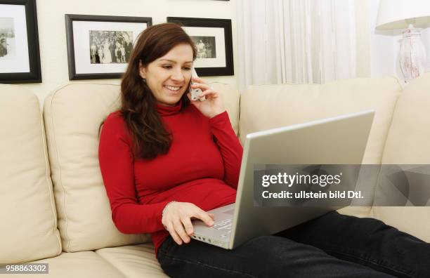 Woman with laptop lying on the sofa is surfing in the internet and making a phone call -