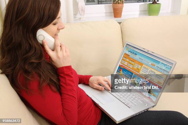 Woman with laptop sitting on the sofa is surfing in the internet on the homepage of the travel agency urlaub.de. -