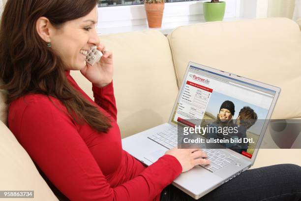 Woman with laptop sitting on the sofa is surfing in the internet on the homepage of the dating agency Partner.de -