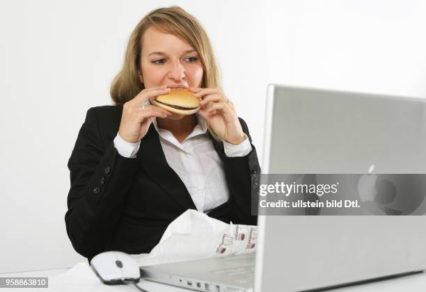 Young woman is working at an apple laptop and is eating a hamburger -