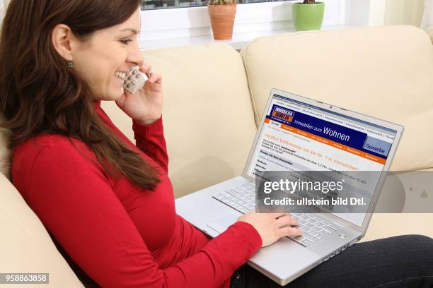 Woman with laptop sitting on the sofa is surfing in the internet on the homepage of real estate platform Immobilienscout24 -