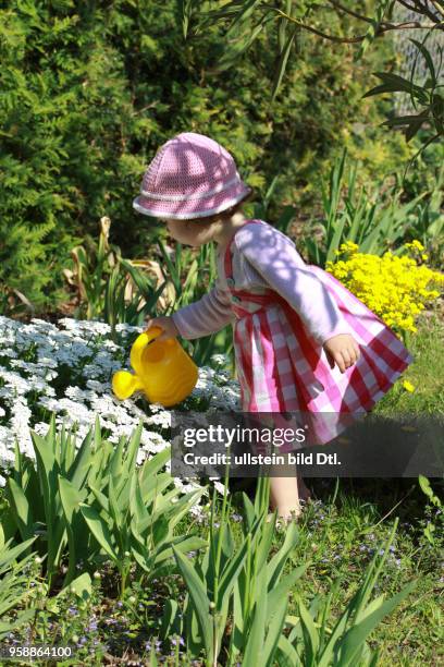 Ein Kleinkind giesst im Garten Blumen