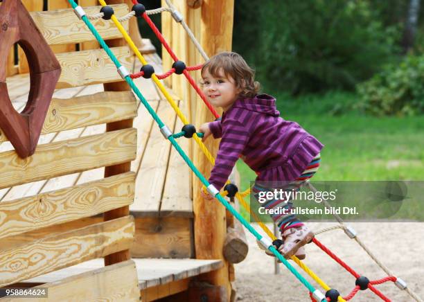 Ein Maedchen klettert an einer Strickleiter auf einem Spielplatz