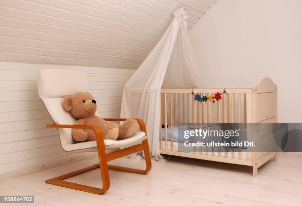 Ein Kinderbett und ein Schwingsessel mit einem Teddybaer stehen in einem Kinderzimmer