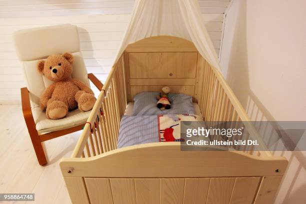 Ein Kinderbett und ein Schwingsessel mit einem Teddybaer stehen in einem Kinderzimmer