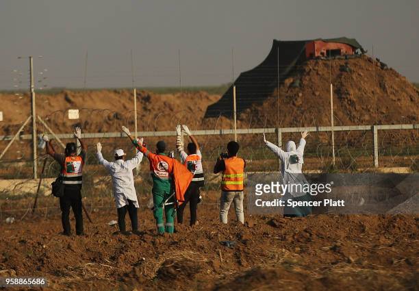 Medical workers raise there hands as they approach the border fence with Israel to retrieve protesters caught in the fence on May 15, 2018 in Gaza...