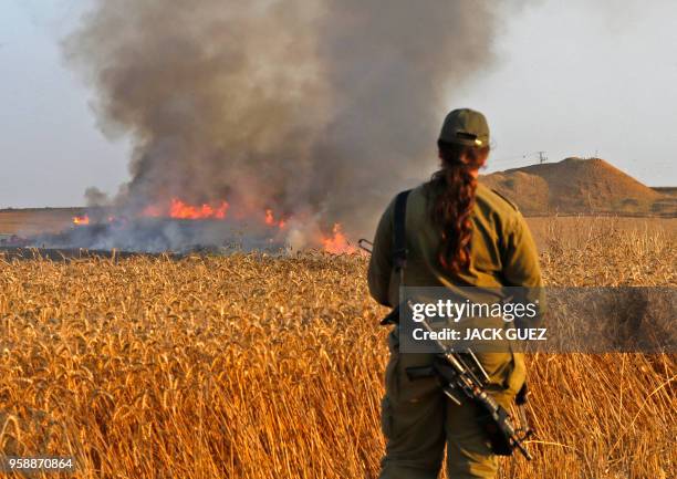 An Israeli female soldier looks at a burning wheat field near the Kibbutz of Nahal Oz along the border with the Gaza Strip, on May 15, 2018 after...
