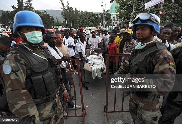 Bolivian UN Blue Helmet soldiers stand guard at an aid center as a group of Haitians carry a victim in Port-au-Prince on January 14 following the...