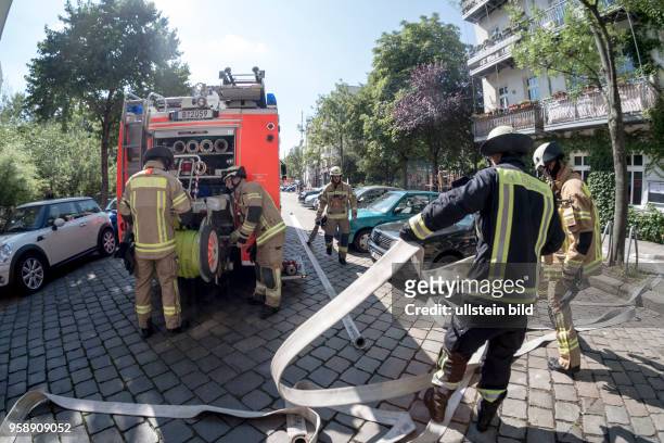 Feuerwehrmänner rollen Schläuche auf die Haspel des Löschfahrzeugs - Einsatz für die Berliner Feuerwehr bei einem vermutlichen Wohungsbrand in...