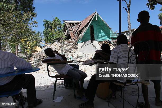 People sit next to a destroyed building in Port-au-Prince, on January 14 following the devastating earthquake that rocked Haiti on January 12....