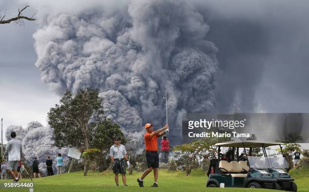 People play golf as an ash plume rises in the distance from the Kilauea volcano on Hawaii's Big Island on May 15, 2018 in Hawaii Volcanoes National...