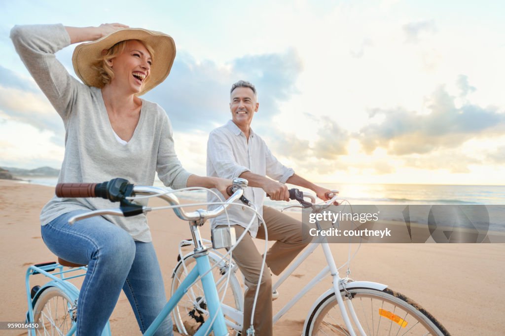 Mature couple cycling on the beach at sunset or sunrise.