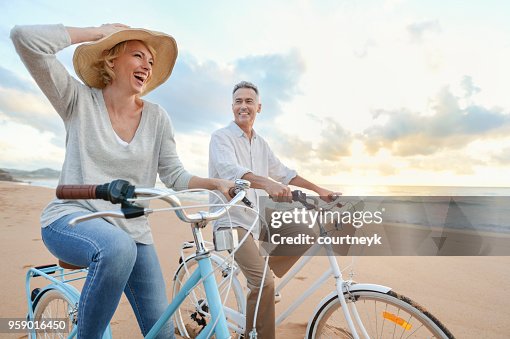 Mature couple cycling on the beach at sunset or sunrise. Mature couple cycling on the beach at sunset or sunrise.